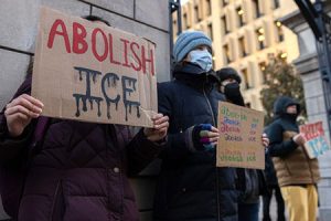 Image of peaceful protestors standing in front of a building holding up signs that read Abolish ICE