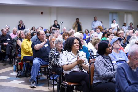 Image of a many people sitting in rows clapping at a meeting of the party
