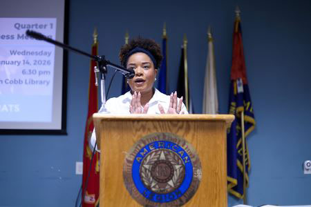 Image of Essence Johnson standing behind a podium with flags behind her