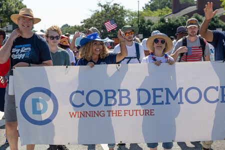 Image of several people in hats standing behind a parade banner that says Cobb Democrats on a sunny day