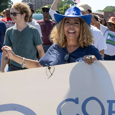 Image of Lucy McBath holding the Cobb Dems sign and others behind her walking in a parade