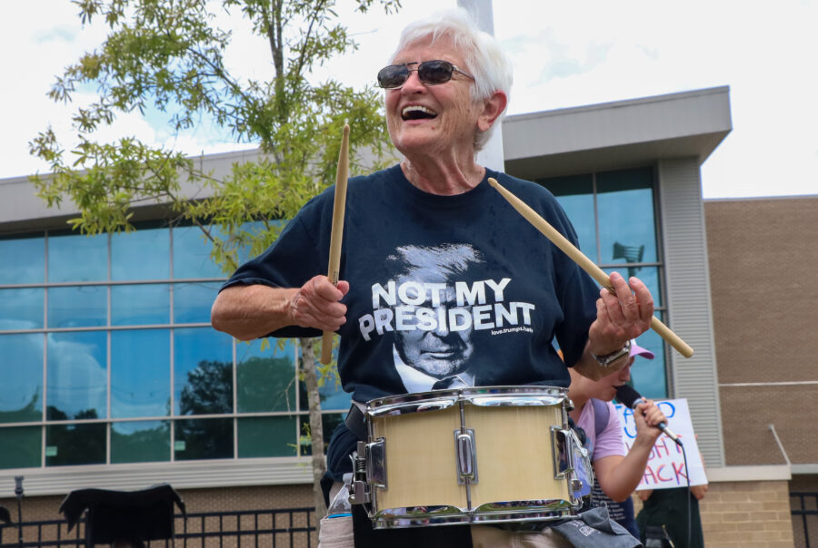 A woman playing a snare drum outdoors. Her shirt says, "Not my President."