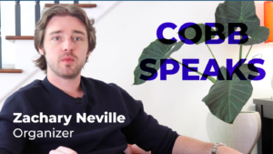A screen grab of a youtube video showing a white man with brown hair sitting next to a plant