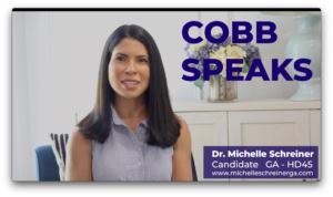 A screen grab of a smiling woman with dark hair. The words Cobb Speaks appears in the top left corner and a title card in the lower left. The title card reads Dr. Michelle Schreiner Candidate GA HD 46 with a campaign url at the bottom.
