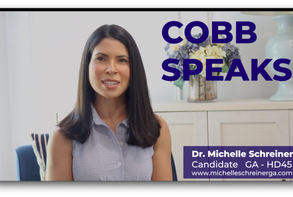 A screen grab of a smiling woman with dark hair. The words Cobb Speaks appears in the top left corner and a title card in the lower left. The title card reads Dr. Michelle Schreiner Candidate GA HD 46 with a campaign url at the bottom.